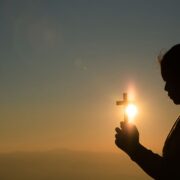 jovem segurando cruz com a luz do sol atras catequista fé frases mensagem