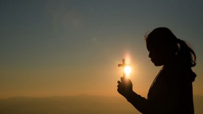 jovem segurando cruz com a luz do sol atras catequista fé frases mensagem