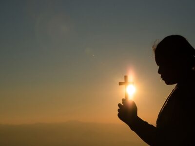 jovem segurando cruz com a luz do sol atras catequista fé frases mensagem