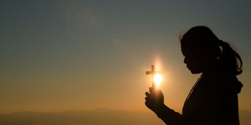 jovem segurando cruz com a luz do sol atras catequista fé frases mensagem